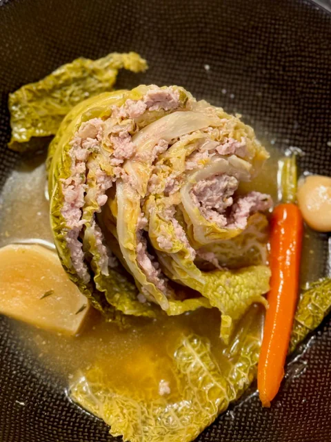 sliced stuffed cabbage in a large bowl surrounded with stock, carrots, garlic and turnip