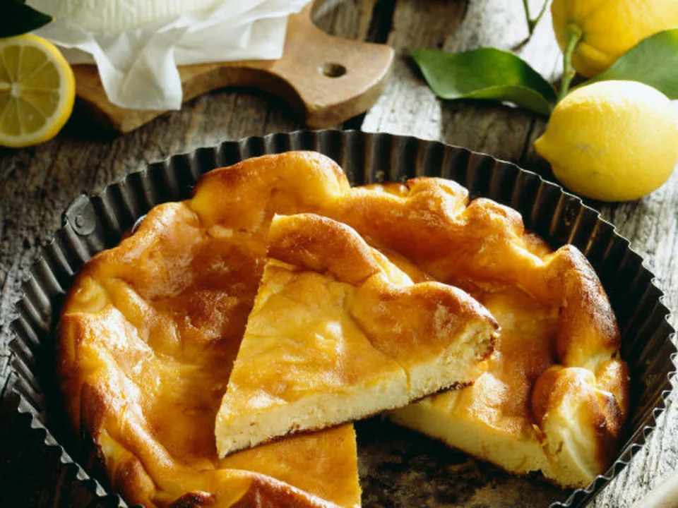 Golden Fiadone in a fluted tin with one slice cut, beside lemons.
