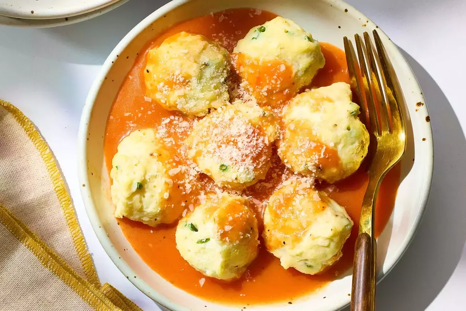 Ricotta dumplings in red pepper-tomato sauce, dusted with Parmesan, on a plate beside a gold fork.